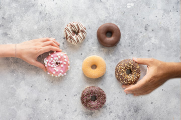 Hands holding  fresh donuts on grey background with copy space. Assortment of various colourful...