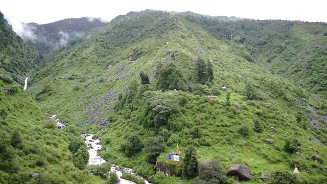 Panning shot showing the lush plant covered mountains and river streams of the himalayas in McLeodganj hill station near Bhagsu Falls