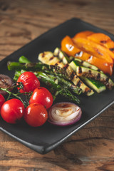 Grilled vegetables assorted on black plate on wooden table background, top view.