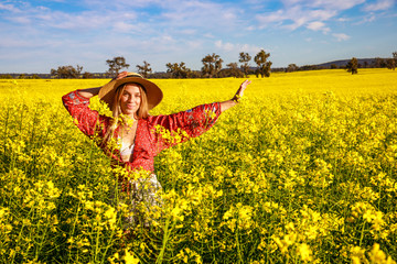Fototapeta premium Happy young lady with straw hat in yellow Canola Field in Western Australia