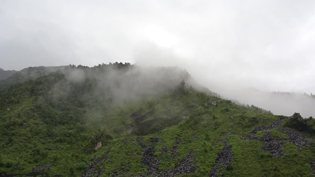 Green plant covered hill with rain falling and a cloud going over the peak in McLeodganj Dharamshala