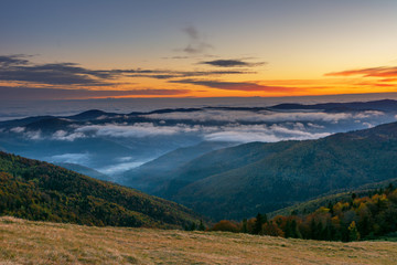 A beautiful autumn dawn in the Ukrainian Carpathian Mountains, with fogs in the valleys and forests, and yellow-red trees.