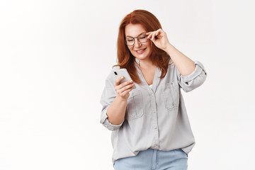 Let look what we got. Gorgeous elegant modern redhead middle-aged mom wear glasses read message check out son send photos social media look smartphone display smiling delighted, white background