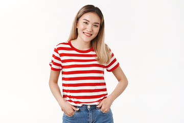 Fototapeta premium Friendly shy cute blond asian female hold hands jeans pockets smiling cheerful tilt head joyfully keep conversation talking campus neighbour standing white background modest asking out girl