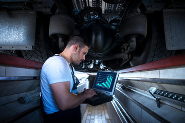 Vehicle mechanic with diagnostic tool laptop working under the truck in workshop. Experienced worker reading parameters and detecting problem. Car or truck service and maintenance. © littlewolf1989