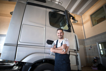 Professional vehicle mechanic standing in workshop with crossed arms and wrench tool ready to start repairing truck. Vehicle service.