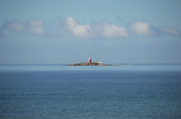 Scenic view of Maddalena or Maddalenetta islet, near Alghero, in Sardinia. It is a red rockof 4 m high, with a red lighthouse. 