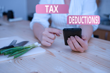 Conceptual hand writing showing Tax Deductions. Concept meaning reduction income that is able to be taxed of expenses woman using smartphone and technological devices inside home