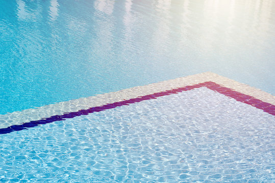 Background of water in blue swimming pool, water surface with a sun reflection