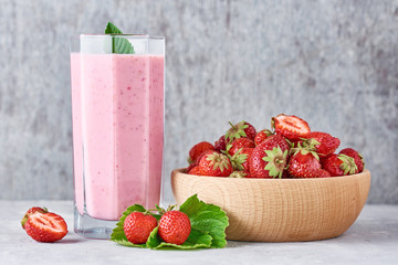 Strawberry smoothie in glass jar and fresh strawberries in wooden bowl on a gray background. Healthy breakfast