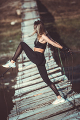 Obraz na płótnie Canvas Attractive young sporty woman is working outside. Cross fit training. Muscular woman. Young, fit and beautiful girl in sporty swimsuit. Sport, diet, health and beauty concept. Young woman in black spo