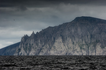 Naklejka na ściany i meble Majestic seascape with a rocky cape. Overcast weather. Epic mountain and sea views. Cape Enmylyn, the coast of the Bering Sea, Chukotka, Russia. Arctic landscape. Russian Far East.