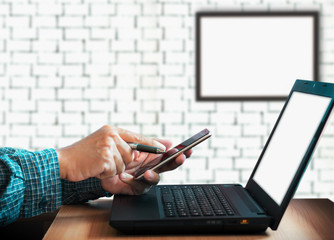 Closeup of hands businessman using smartphone and laptop working online with blur white brick wall background