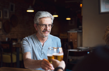 Senior man toasting with a beer in a bar