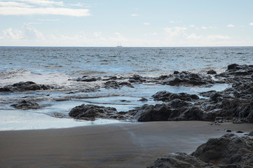 Fototapeta premium View of a beautiful remote volcanic sand beach with tranquil waves hitting rocks and sand, on a cloudy day, after the storm, on the northern coast of the island of Tenerife, Canary Islands, Spain