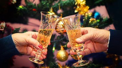 Senior couple hands celebrating Christmas by toasting glass of champagne at home