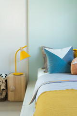 Kid bedroom in blue and yellow tone pillow with many doll on bed. 