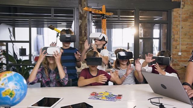 Group of happy young pupils of elementary school using virtual reality headsets during computer coding class
