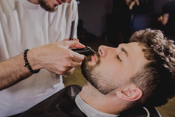 Young man with trendy haircut at barber shop. Barber does the hairstyle and beard trim.