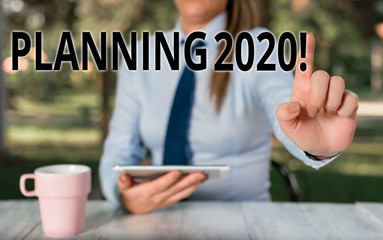 Conceptual hand writing showing Planning 2020. Concept meaning process of making plans for something next year Female business person sitting by table and holding mobile phone