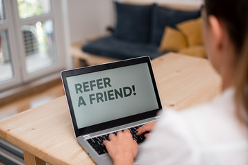 Conceptual hand writing showing Refer A Friend. Concept meaning direct someone to another or send him something like gift woman with laptop smartphone and office supplies technology