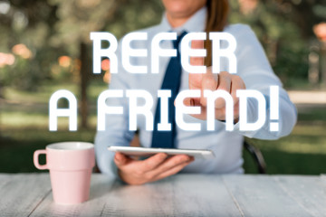 Text sign showing Refer A Friend. Business photo text direct someone to another or send him something like gift Female business person sitting by table and holding mobile phone