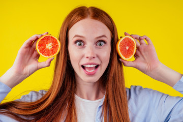 redhaired ginher woman holding red hybrid orange in studio yellow background