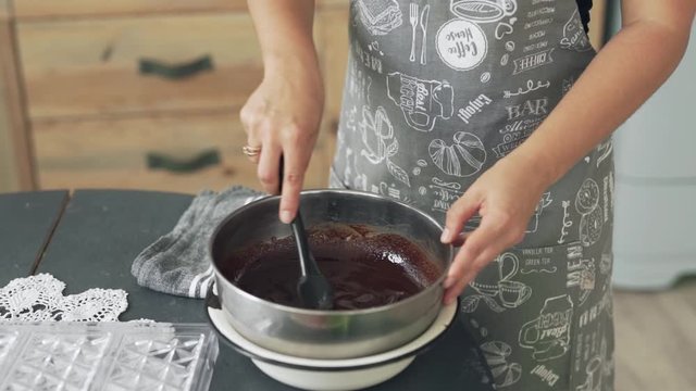 Close up of woman in apron mixing melted chocolate in kitchen scene