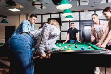 Young woman playing in billiard. Posing near the table with a cue in her hands