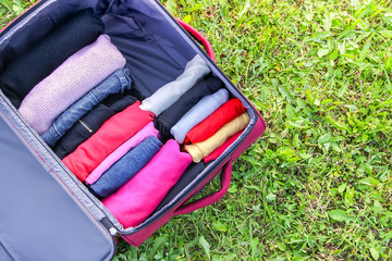 Open suitcase on the green grass with different clothes folded vertically. Vertical storage for easy travel packing.