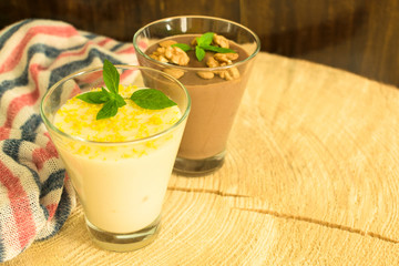 Dessert, chocolate pudding with nuts and vanilla pudding with lemon zest on a wooden background.
