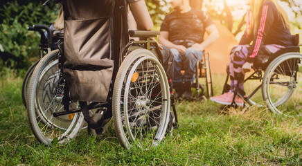 Obraz premium Disabled man resting in a campsite with friends. Wheelchair in the forest on the background of tents