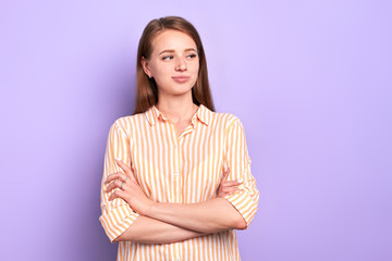 Fototapeta premium Studio portrait of thoughtful pretty young woman with contemplative face expression, looking aside with light smile, thinking about oncoming date with her boyfriend, isolated over purple wall.