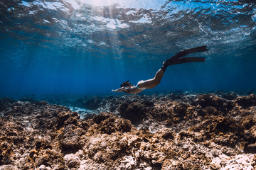 Free diver woman with fins glides over corals in blue sea.