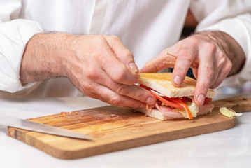 Chef finalizes the sandwich with ham and salad on the wooden board .