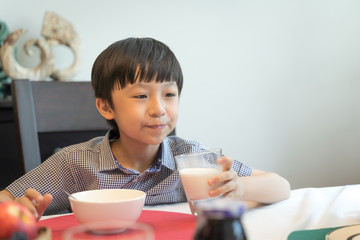 The boy is eating milk and breakfast at home.