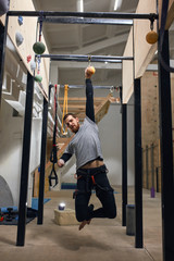 Obraz na płótnie Canvas Cheerful handsome rock climber with physical disability training at chin up bar, hanging on one hand at suspended ball, doing special exercises for strength and endurance. Vertical shot, front view.