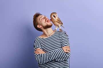 funny crazy man with crossed arms putting tongue out, looking at the owl, close up portrait,...