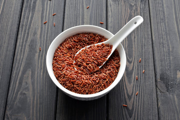 red rice in a ceramic bowl with spoon against dark wooden background