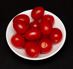 Red cherry tomatoes in a white plate on a black background