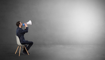 Obraz premium Businessman staying in an empty grey dark room with stuffs on his lap