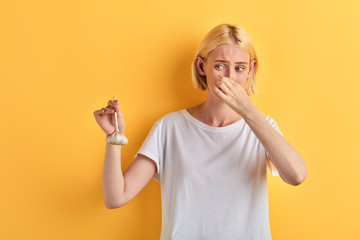 beautiful young woman in white t-shirt closing her nose with fingers, isolated yellow background,...