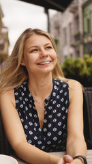 Portrait of smiling blonde sitting at coffee shop near green plants - summer