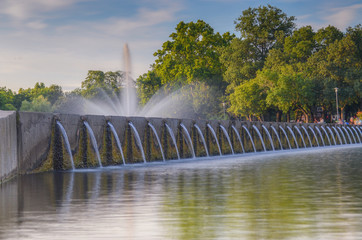 Long exposure landscape photo of water fountain in a city park tourism with sky and tree behind