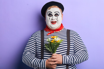 positive funny mime with a bunch of wonderful flowers posing to the camera, isolated blue...