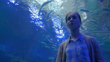 Portrait of woman looking at fish vortex in large public aquarium tank at Oceanarium. Tourism, education, underwater life and entertainment concept