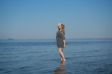 Fototapeta na wymiar Attractive plus size woman in chiffon dress enjoys the shiny water in the blue sea