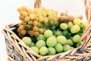 Green and blue grapes in a wicker basket on white background, autumn harvest.