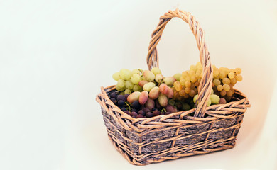 Green and blue grapes in a wicker basket on white background, autumn harvest.