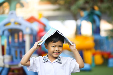 An Asian boy put a book on his head with smiling in a school.